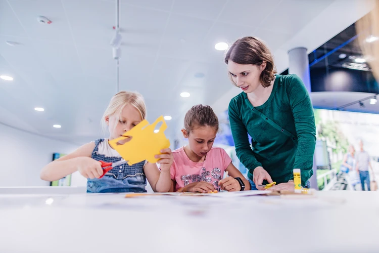 Zwei M&auml;dchen beim Basteln, angeleitet von einer Besucherbetreuerin der KLIMA ATRENA.