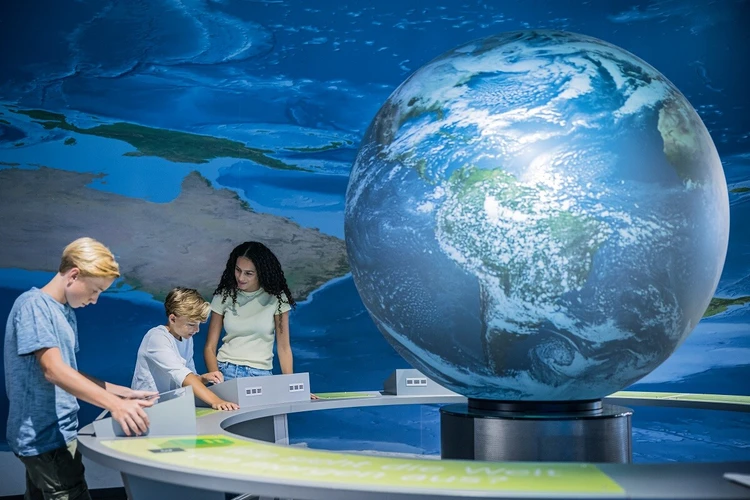 Das Foto zeigt Kinder und Jugendliche, die in einer Ausstellung an einem interativen Tisch mit einem gro&szlig;en Globus zum Thema Klimaschutz arbeiten.
