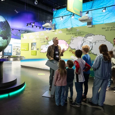 Familie mit Besucherbetreuer bei F&uuml;hrung am interaktiven Globus.