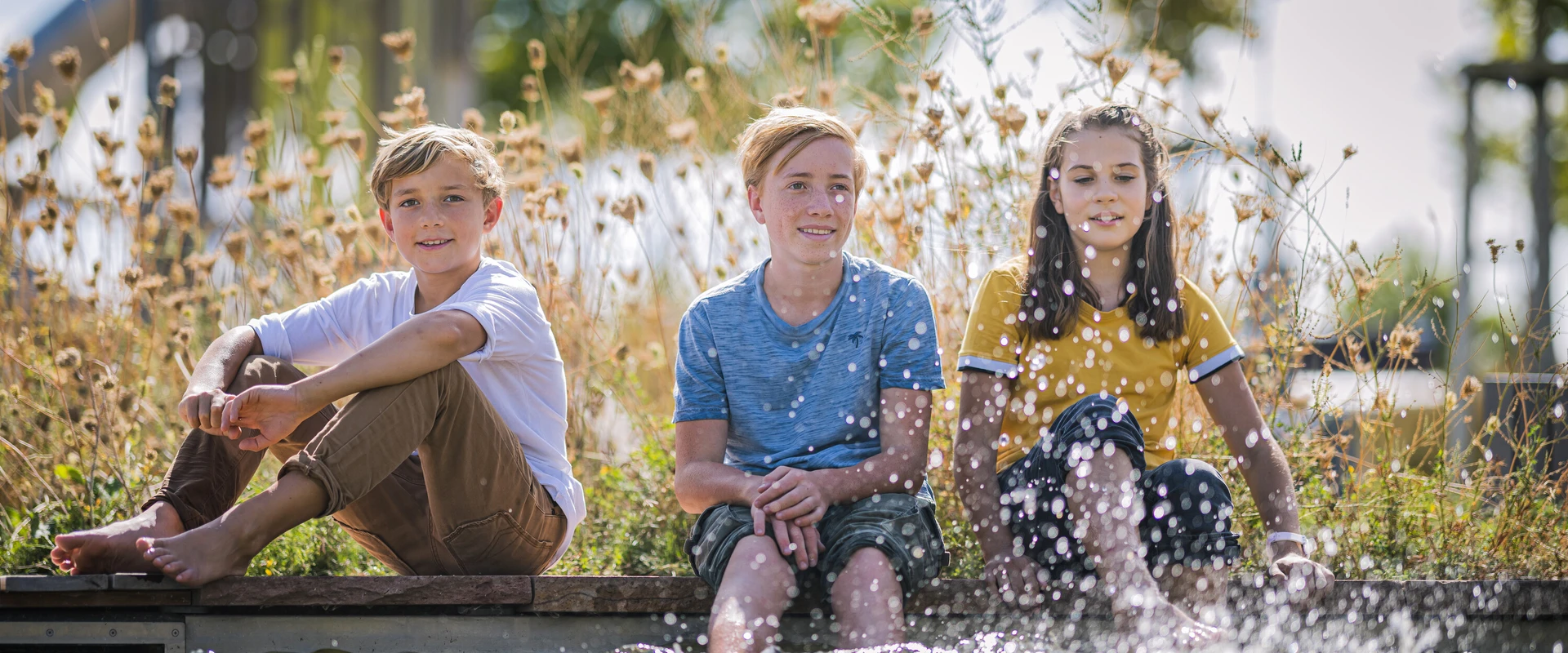 Kinder sitzen am Rand einer Wasserfl&auml;che und strecken die F&uuml;&szlig;e ins Wasser.