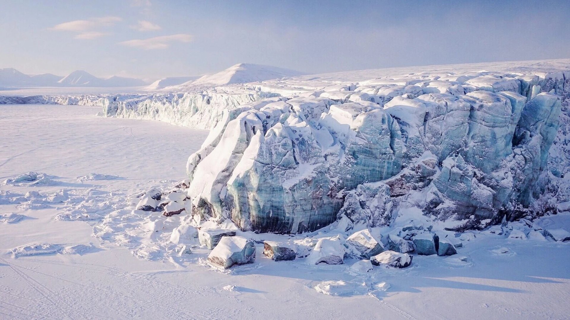 Blick auf ein Eisgebirge von oben, davor f&auml;hrt ein Schneemobil auf einem Eisfeld.