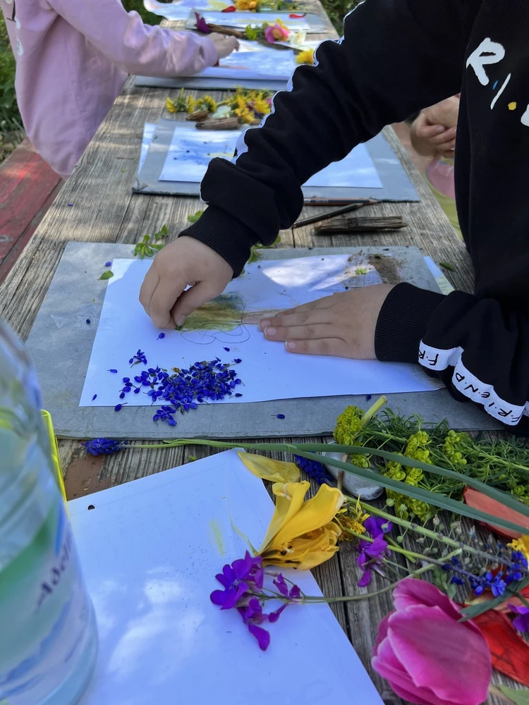 Auf dem Bild sind Kinderh&auml;nde zu erkennen, sie auf einem Blattpapier mir bunten Bl&uuml;tenbl&auml;ttern basteln.